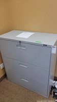 Metal gray filing cabinet with three drawers and a key lock on top drawer