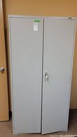Front view of tall gray metal cabinet with two doors and a lock on the right door.