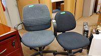 Photo showing two adjustable office chairs side by side, one blue with armrests, and one black without armrests, in an office setting.