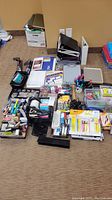 Photo showing the large assortment of office supplies spread on the floor including binders, clipboards, writing instruments, stamps, labels, tape, and other office essentials.