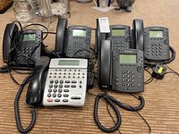 Lot of five Polycom BVX311 phones and one NEC Dterm 80 phone placed on carpet. Shows overall condition and inclusion of cords.
