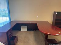 Cherry wood office desk with three connected sections forming a U-shaped workspace in an office setting next to window.