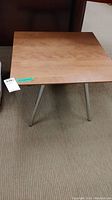 Square wood table with metal legs on carpeted floor, showing the top and legs from a top front angle