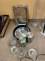 Photo showing entire lot including glass jars, metal canisters, serving trays, and the glass vase on carpet floor.