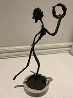 Side view of elongated bronze female figure on circular marble base, showing texture and pose