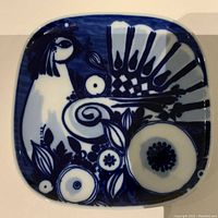 Top view of a square blue and white ceramic plate showing a detailed abstract peacock and floral design.