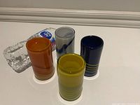 Set of four small vintage Finnish blown glass vases arranged in a row with a bottle for size comparison