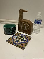 Photo showing all three vintage decor items together with water bottle for scale: brown bird-shaped sculpture, green ceramic bowl, and colorful tile with floral pattern.