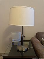 Ridgefield Nickel buffet lamp by Ethan Allen on a glass side table next to a sofa, showing full lamp with shade and base.