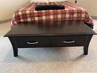 Black wood coffee table with two silver-handled drawers in front and gently curved legs.