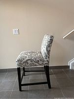Side profile view of a single counter stool showing upholstery, frame and stretcher detail