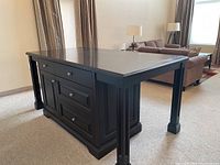 Front view of custom dining table island showing cabinet doors and drawers with metallic knobs, detailed panel legs, and dark finish.