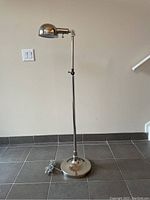 Full view of the Sullivan nickel floor lamp from Ethan Allen showing the lamp standing on tiled floor against a light wall, with cord coiled at base.