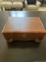 Top view of closed wood jewelry box with scalloped edges and brass handles