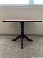 Front view of the small wooden square table showing the pedestal base with four curved legs and turned central column.