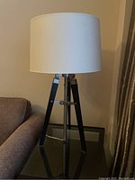 Tripod table lamp standing on glass-top table next to sofa and curtain backdrop