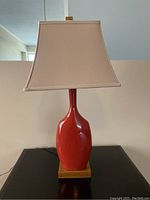 Photo of one red ceramic table lamp with beige shade and wooden base