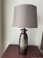 Single bronze metallic finish table lamp with vertical ribbed pattern and beige drum shade