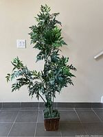 Front view of artificial tree showing dense realistic green variegated leaves and multiple slender stems in a brown woven-style square pot.