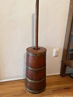 Full view of the tall wooden butter churn with handle, showing the exterior wooden barrel and metal bands.
