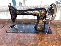 Black Singer sewing machine head showing gold decals, handwheel and needle area