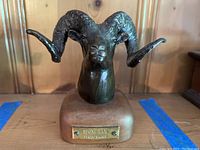 Front view showing ram head sculpture on wooden base with brass plaque reading 'Stone Ram by Carl Wagner'