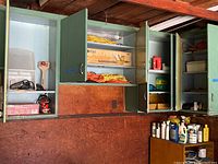 Four green garage cabinets with open doors showing contents including cords, tools, and boxes.