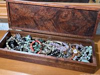 Wood box open showing all jewelry items inside including bracelets, necklaces, pendants, and watch.
