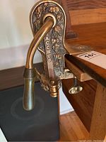 Close-up showing the embossed Bacchus name and grapevine decoration on the brass wine opener handle and body mounted to a wooden counter or desk edge.