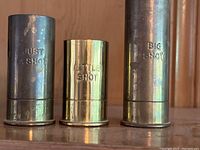Front view of three faux shotgun shell shot glasses with engraved labels LITTLE SHOT, JUST A SHOT, and BIG SHOT.