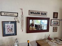 Full view of all nine wall decor pieces arranged including the large mirror and signs, framed embroidery, and assorted smaller framed pictures