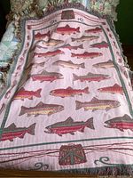 Full view of the handmade fish blanket showing multiple fish motifs and fishing themed border in pink, green, and red colors on a bed.