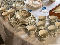 Full view of the partial dinnerware set including stacked plates, bowls, cups, and saucers arranged on a table, showing green floral patterns on white ironstone.