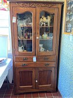 Full view of wooden kitchen cabinet with glass doors displaying decorative items inside shelves, three drawers below, and lower two-door section.