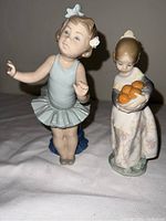 Two Lladro porcelain figurines: a ballerina in a light blue tutu and a girl in a floral dress holding oranges.