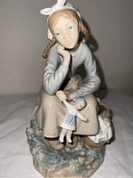Front view of Lladro porcelain figurine of a seated girl holding a doll and basket of fruit.