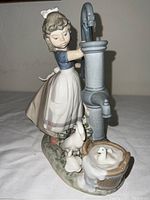 Side view of the figurine showing the girl operating the water pump with ducks near the base.