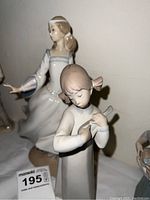 Photo showing two Lladro girl figurines with soft lighting and white fabric background, highlighting the delicate porcelain and coloring.