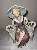Front view of seated woman figurine with wide-brimmed hat holding pink parasol on an ornate white bench