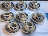 Full view of all eight bird-shaped ceramic egg cups on matching saucers, arranged on white cloth.