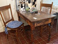 Wide view showing the rectangular vintage wooden table with two matching chairs on either side, one with blue cushion tied to seat.