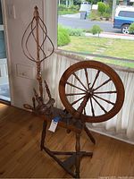 Full view of the vintage wooden spinning wheel showing the tripod base, large spoked wheel and spindle accessory.