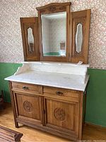 Front view of vintage wood dresser with white marble top, three-way mirror with two side panel mirrors, carved basket designs on cabinet doors and drawers, showing overall condition and style.