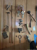 Wide view of wood backboard showing spurs, horseshoe, horse bit, powder horn, whisk, meat hook, toaster rack