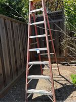 Full view of the Werner fiberglass step ladder standing outdoors against a wooden fence, showing fiberglass rails and aluminum steps.