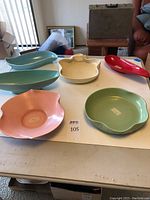 Six vintage pottery pieces in various pastel and bright colors arranged on a table.
