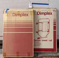 Two Dimplex branded cardboard boxes, one with red printed product illustration and branding, showing packaging of electric towel warmers
