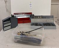 Overall view of two metal cases, one plastic case, and a bin of loose drill bits on table.