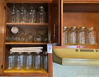 Wooden cabinet shelf displaying multiple clear glass jars on two shelves
