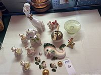 Overview of the entire lot showing all porcelain animal figurines, glass dish, fish family pieces, brass Eiffel Tower and Asian bowl.